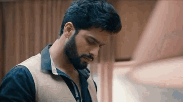 a man with a beard is wearing a vest and a black shirt .