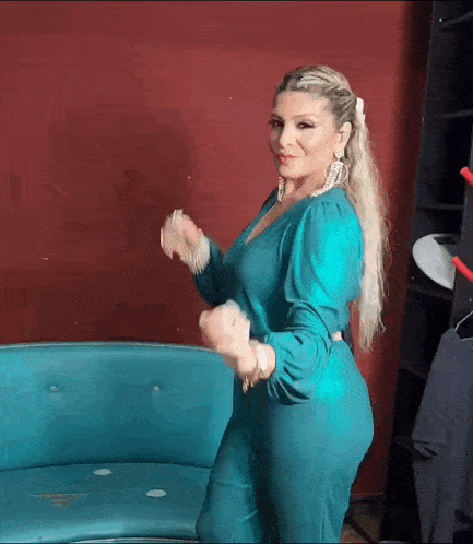 a woman in a blue jumpsuit is standing next to a blue couch and dancing .