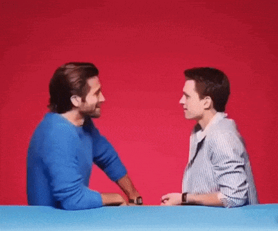 two men are standing next to each other at a table and talking to each other .