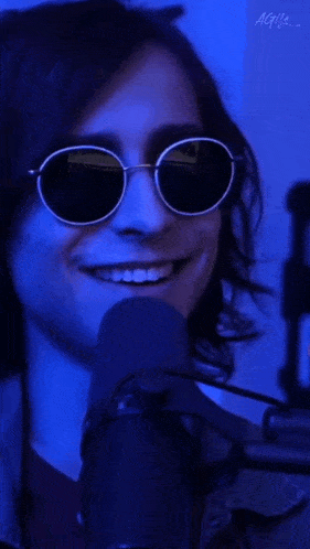 a man wearing sunglasses is smiling in front of a microphone and the word funny is on the bottom right