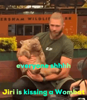 a man is holding a wombat in front of a sign that says ' everyone shhhh '
