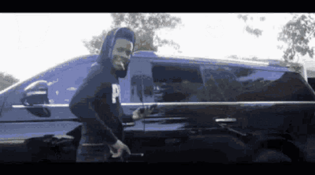 a man in a hoodie is standing in front of a black suv
