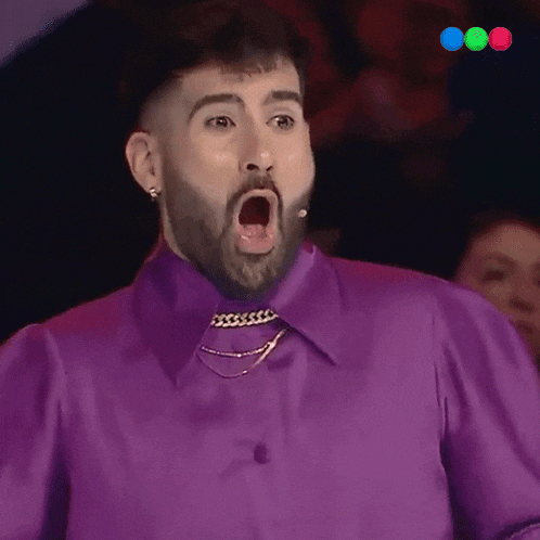 a man with a beard is wearing a purple shirt and making a surprised face