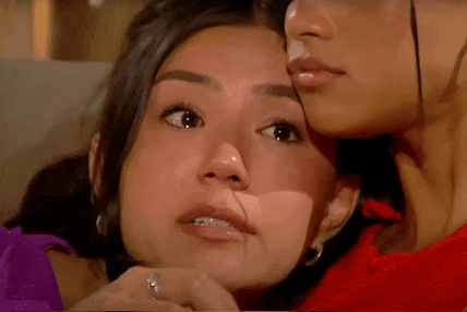 two women are sitting next to each other on a couch and one woman is whispering into the other 's ear .