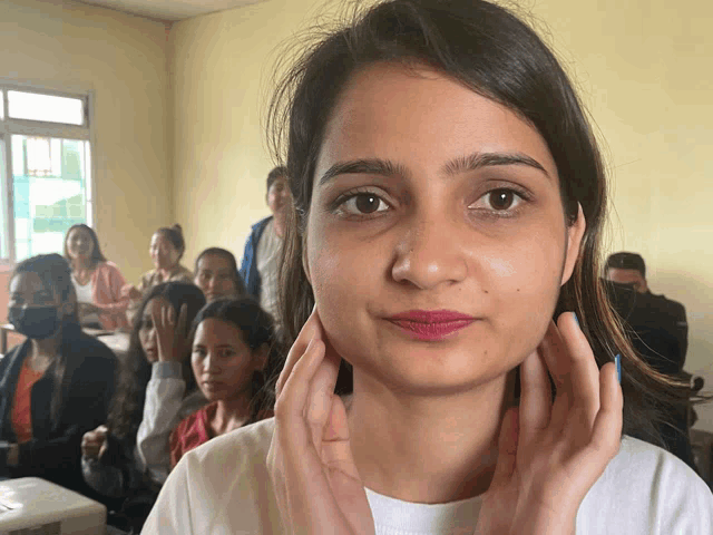 a woman with pink lipstick holds her hands to her face in front of a group of people