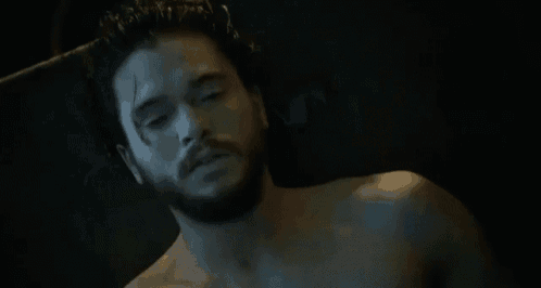 a shirtless man with a beard is laying in a dark room with a black background .