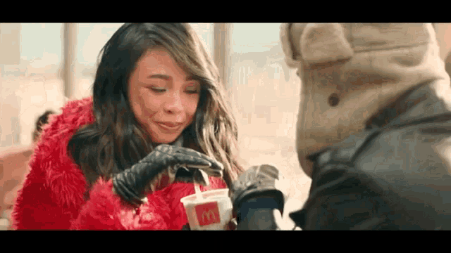 a woman in a red fur coat is drinking through a straw from a mcdonalds cup .