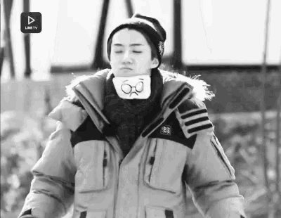 a black and white photo of a person wearing a jacket , hat , scarf and glasses .