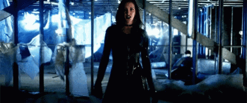 a woman in a black suit is standing in a building holding a sword .