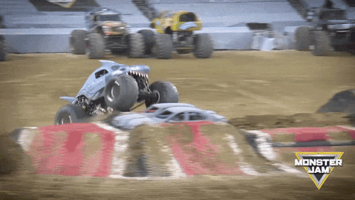 two monster trucks are racing on a dirt track with a monster jam logo in the foreground
