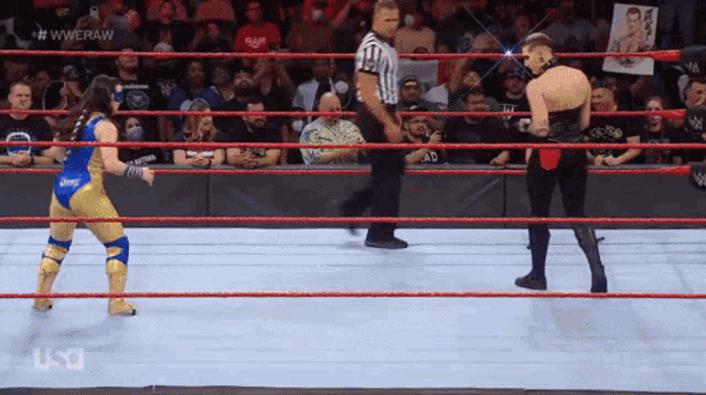 two wrestlers are in a wrestling ring with a referee and a crowd watching .