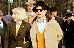 a man wearing sunglasses and a hat is standing next to a woman in a suit
