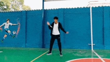 a young man is dancing on a basketball court in front of a mural of a soccer player on a wall .