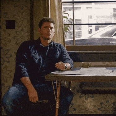 a man is sitting at a table in front of a window with flowers on the wall .