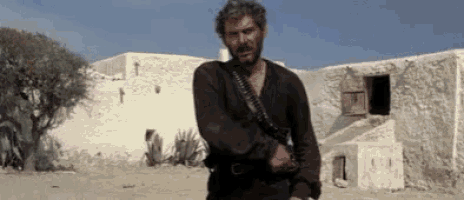 a man with a beard is standing in front of a building holding a gun