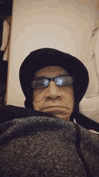 a man wearing glasses and a hooded jacket looks at the camera