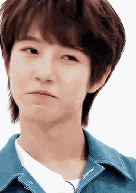 a young man wearing a blue denim jacket and a white t-shirt is making a face .