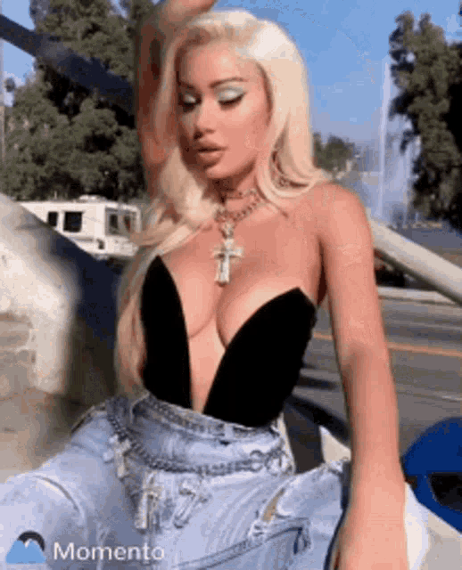 a blonde woman wearing a black top and blue jeans is sitting on a car .