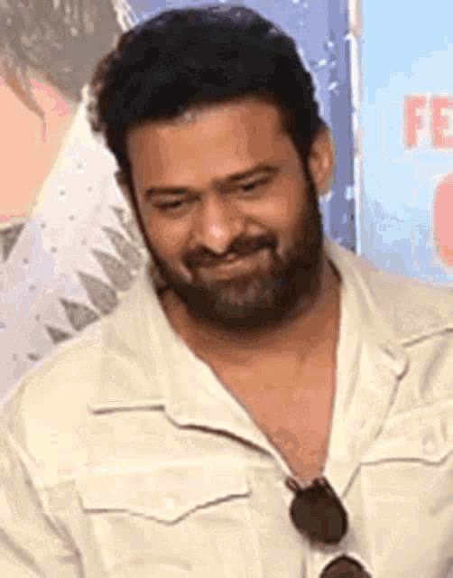 a man with a beard is wearing sunglasses and a white shirt and smiling .