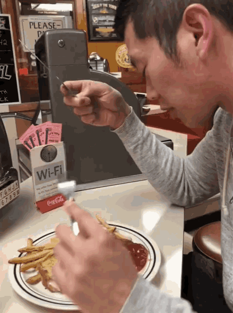 a man eating french fries in front of a wi-fi sign