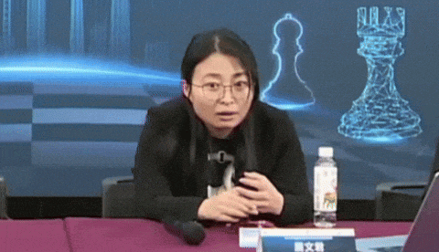 a woman sitting at a table with a bottle of water and a chess piece in the background
