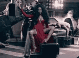 a woman in a red dress is sitting on a suitcase on the street .
