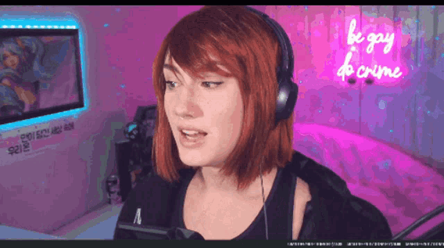 a woman wearing headphones stands in front of a neon sign that says be gay be crime