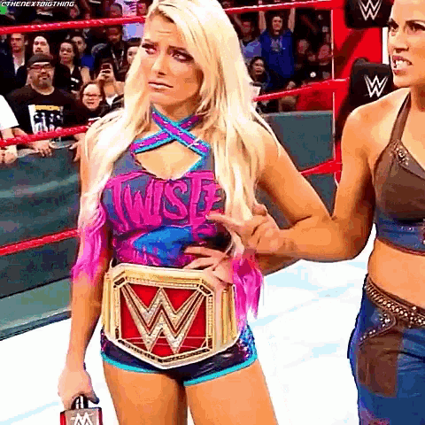 a female wrestler is standing in a wrestling ring holding a championship belt .