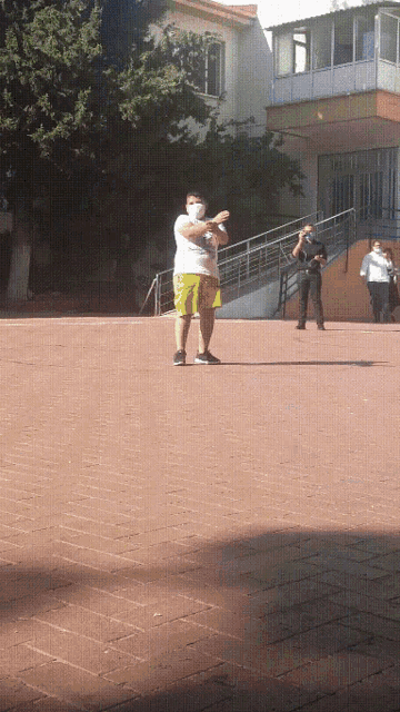 a man in a white shirt and yellow shorts is standing on a brick pavement