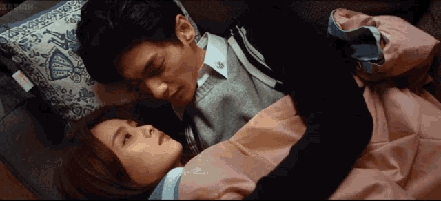 a man and a woman are laying on a bed and the man is wearing a grey sweater with the letter e on it