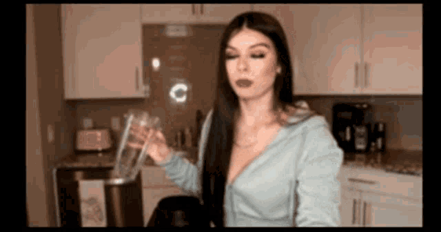 a woman is pouring a glass of water into a pitcher in a kitchen .