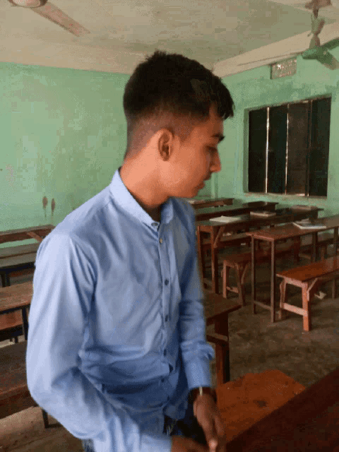 a young man in a blue shirt is sitting in a classroom