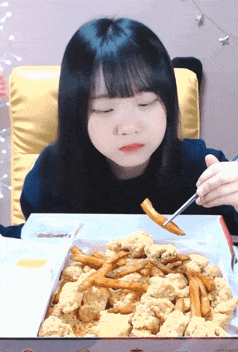 a girl with her eyes closed is eating fried chicken and french fries