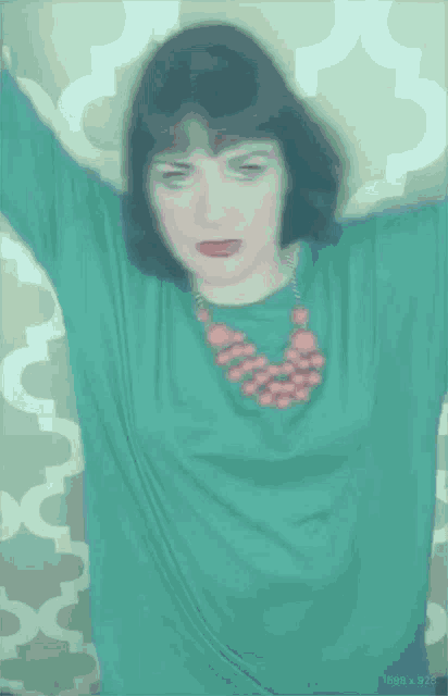 a woman wearing a green shirt and a pink necklace is making a face .