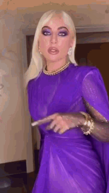 lady gaga is wearing a purple dress with a cape and a necklace .