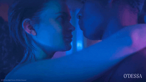 a man and a woman are kissing in a dark room with blue lights behind them