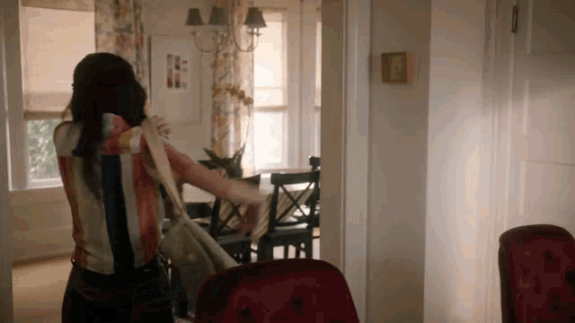 a woman in a striped shirt is standing in a dining room holding a purse .