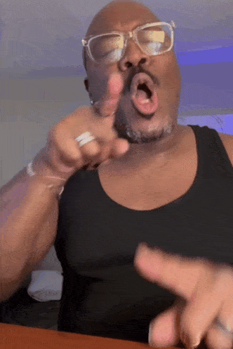 a man wearing glasses and a black tank top is pointing at the camera .