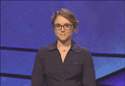 a woman wearing glasses and a black jacket is smiling while standing on a stage .