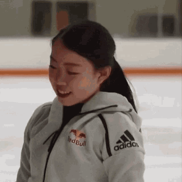 a woman wearing a white jacket with the word adidas on the sleeve is standing on a ice rink .