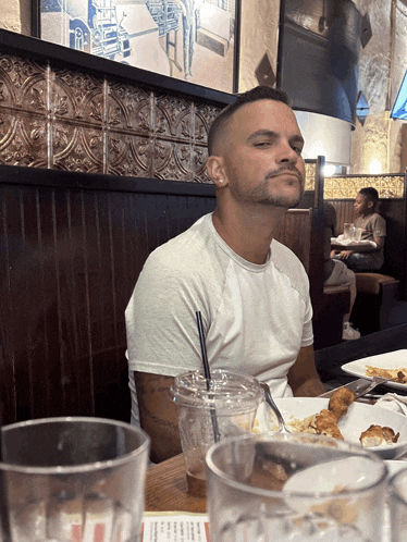a man sits at a table in a restaurant with his eyes closed and a drink in his hand