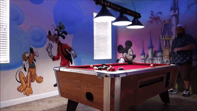 a pool table with mickey mouse and goofy on the wall behind it