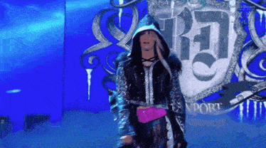 a woman in a hooded jacket stands in front of a shield that says rj on it
