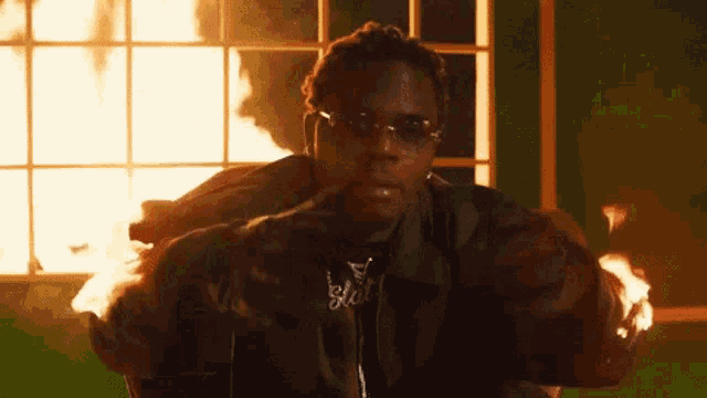 a man wearing sunglasses is sitting in front of a window with a fire coming out of it .
