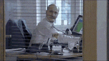 a man is sitting at a desk with a glass of wine in front of him