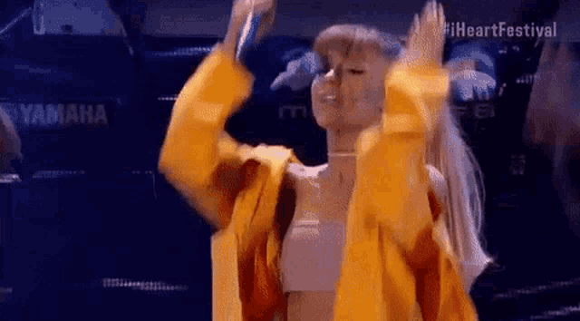 ariana grande is wearing a yellow jacket and holding a microphone on stage .