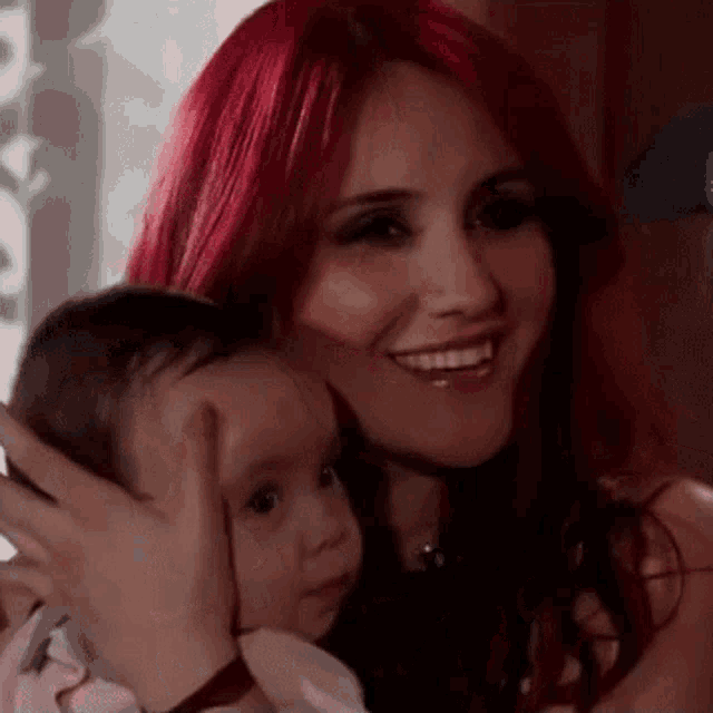 a woman with red hair is smiling while holding a baby .