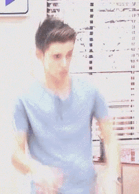 a young man in a blue shirt is standing in front of a window with blinds