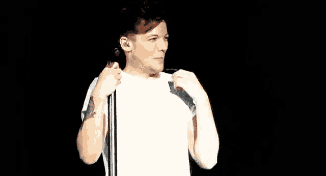 a man in a white t-shirt is standing in front of a microphone .