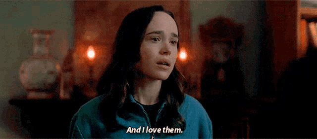 a woman in a blue jacket is standing in a dark room and saying `` and i love them . ''